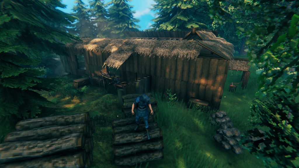 Valheim screenshot. My newes building, mostly looking like a big, wooden block. Forge to the side with walls and chests indcating the outline of a further room. In the front are piles of stone and wood.